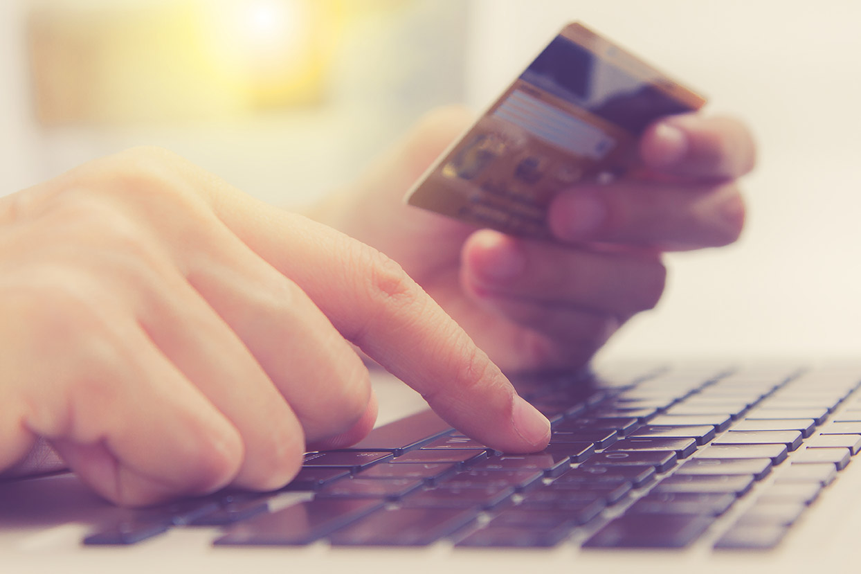 A hand holds a credit card, while the other hand types the numbers into an e-commerce site