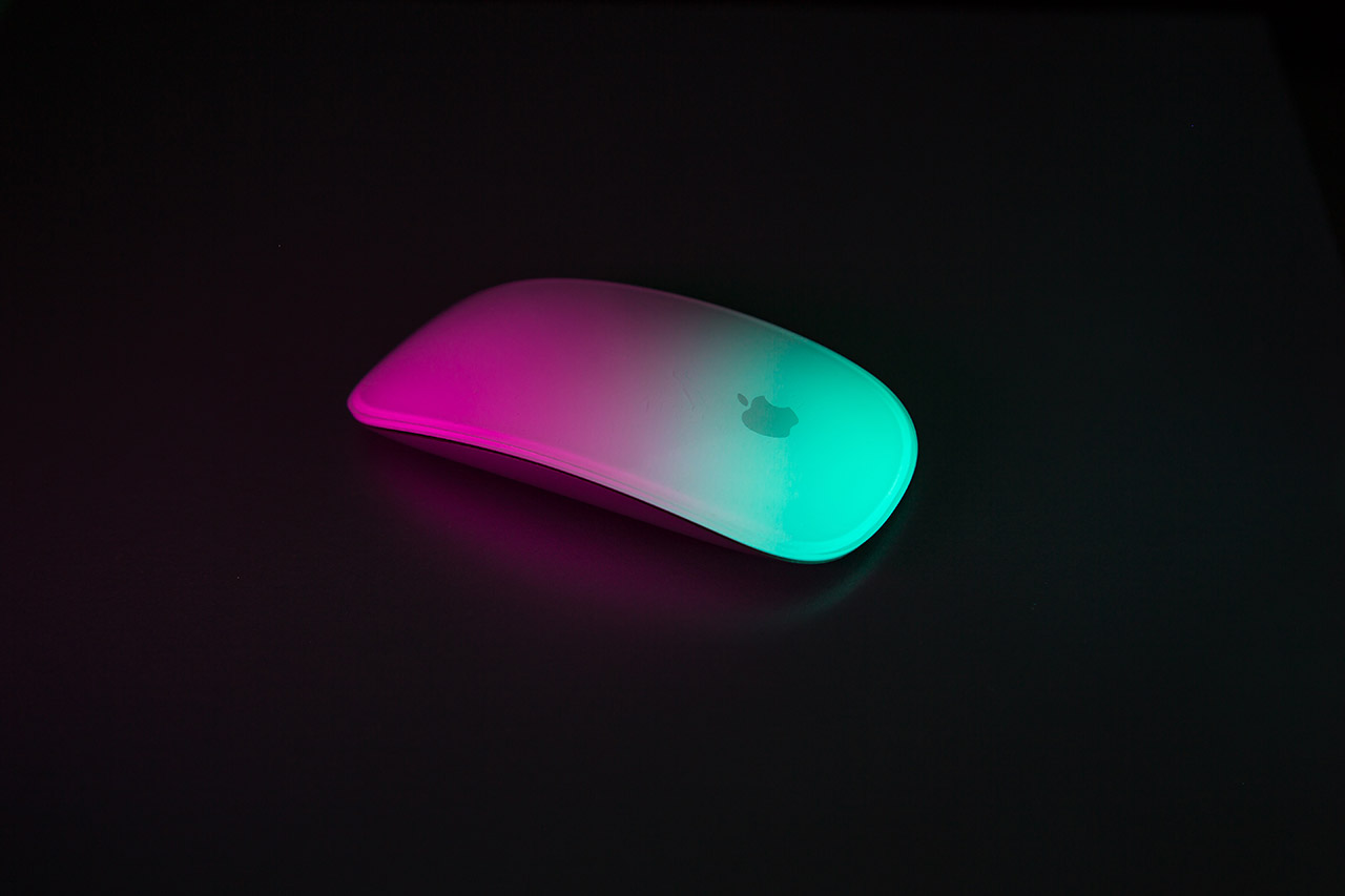 A computer mouse on black, highlighted by pink and teal light.